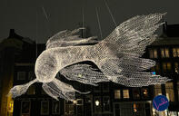 Illuminated fish-shaped light sculpture suspended above the canal during the Amsterdam Light Festival.