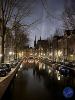 View of Amsterdam canal at night with bridges lit by festive lights and historic houses reflected in the water.